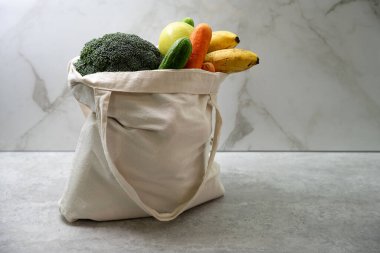 Eko yeniden kullanılabilir kumaş alışverişi ve içi taze sebzelerle dolu bir çanta mutfak tezgahında duruyor. Sürdürülebilir yaşam tarzı.