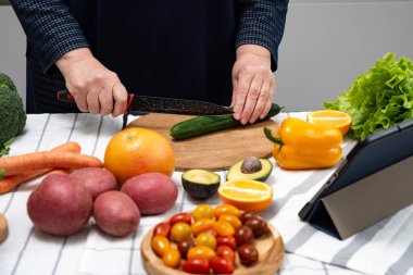 Olgun bir kadın internette tabletle yemek pişiriyor. Yemek zamanı.