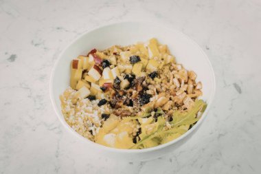 Mermer bir yüzey üzerinde sebze, tahıl ve baklagiller de dahil olmak üzere çeşitli sağlıklı malzemelerle dolu beyaz bir kase..