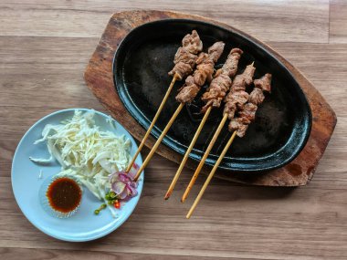 An overhead shot of Indonesian Sate Maranggi (grilled beef skewers) served sizzling on a cast iron plate, accompanied by a side of shredded cabbage, chopped shallots, chilies, and soy sauce.