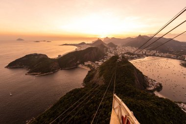 Sugar Loaf dağından Rio de Janeiro, Brezilya 'daki tramvaya, şehre ve okyanusa güzel altın gün batımı manzarası