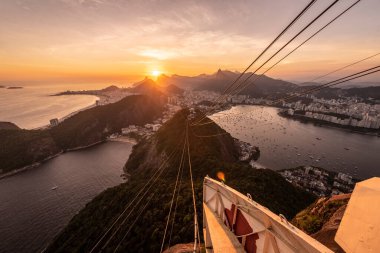 Sugar Loaf dağından Rio de Janeiro, Brezilya 'daki tramvaya, şehre ve okyanusa güzel altın gün batımı manzarası