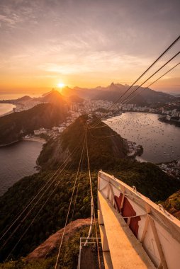 Sugar Loaf dağından Rio de Janeiro, Brezilya 'daki tramvaya, şehre ve okyanusa güzel altın gün batımı manzarası