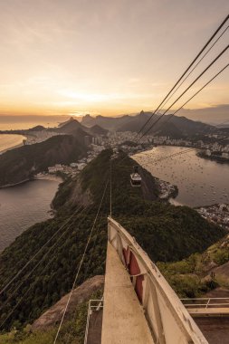 Sugar Loaf dağından Rio de Janeiro, Brezilya 'daki tramvaya, şehre ve okyanusa güzel altın gün batımı manzarası