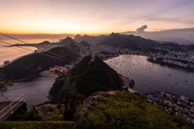 Sugar Loaf dağından Rio de Janeiro, Brezilya 'daki tramvaya, şehre ve okyanusa güzel altın gün batımı manzarası