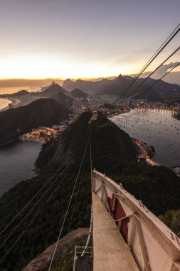 Sugar Loaf dağından Rio de Janeiro, Brezilya 'daki tramvaya, şehre ve okyanusa güzel altın gün batımı manzarası