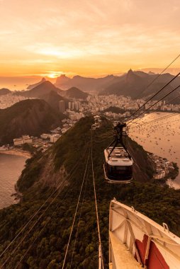 Sugar Loaf dağından Rio de Janeiro, Brezilya 'daki tramvaya, şehre ve okyanusa güzel altın gün batımı manzarası
