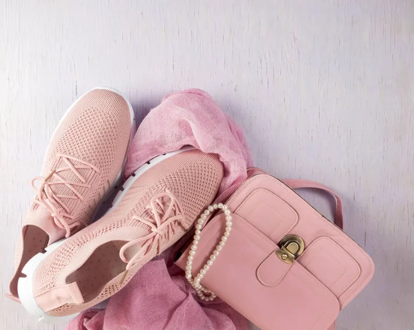 Things are laid out on a lilac, wooden background. A small pink handbag and light summer shoes. Layout on the table.