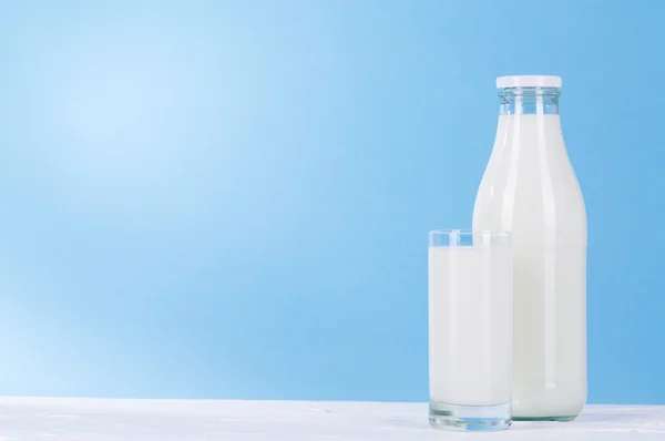 Bottiglia e bicchiere di latte su fondo blu . — Foto Stock