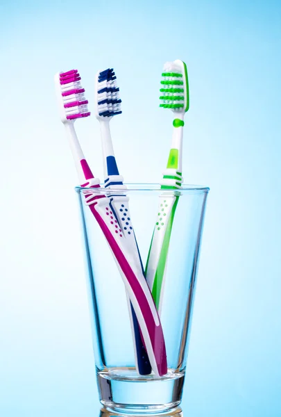 Cepillos de dientes en vidrio sobre fondo azul claro . — Foto de Stock