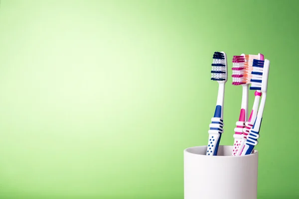 Toothbrushes in white cup on light green background — Stock Photo, Image