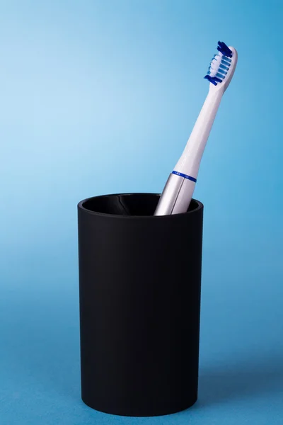Tandenborstel in zwarte cup op blauwe achtergrond — Stockfoto
