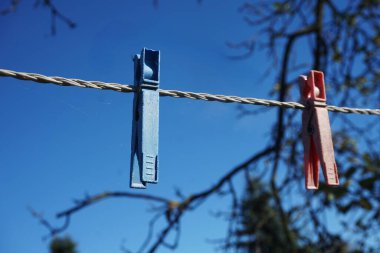 Parlak bir gökyüzünün altında çamaşır ipinde asılı renkli mandallar ve çiviler. Görünürde çamaşır yok, sadece güneş ışığında klipler var..