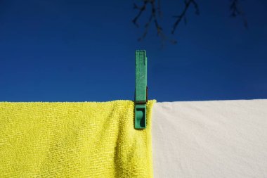 Çamaşır mandalı sıcak ve güneşli bir günde çamaşır ipini kurutur. Yakın çekim kumaş dokusunu ve hoş yaz atmosferini ön plana çıkarıyor..