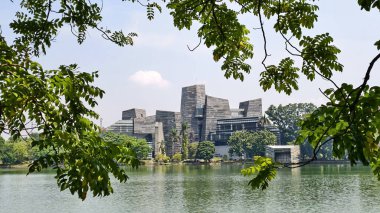 modern building with unique architectural design beside a lake with blue sky, with reflection in the water. the central library of the university of indonesia