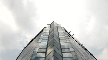 Modern cam binanın ön cephesinin düşük açılı görüntüsü bulutlu bir gökyüzüne karşı mimari tasarımını vurguluyor. gökdelen