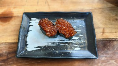 Yakından çekilen bir fotoğraf canlı ikura suşisinin ince detaylarını yakalar. Dolgun, şeffaf portakal renkli somon balığı yumurtası baharatlı pirincin üzerinde parlar..