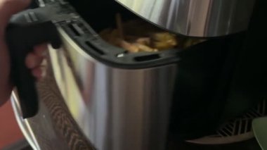 Bir insan kızartma makinesini açar ve pişirirken kızarmış patates kızartması karıştırır. Altın patatesler eşit derecede kızarır, ev yapımı sağlıklı fast food hazırlıklarını gösterir..