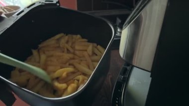 Bir insan kızartma makinesini açar ve pişirirken kızarmış patates kızartması karıştırır. Altın patatesler eşit derecede kızarır, ev yapımı sağlıklı fast food hazırlıklarını gösterir..
