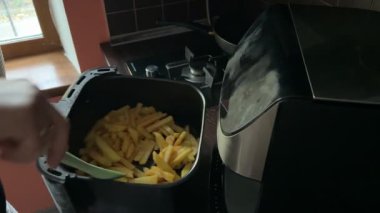 Bir insan kızartma makinesini açar ve pişirirken kızarmış patates kızartması karıştırır. Altın patatesler eşit derecede kızarır, ev yapımı sağlıklı fast food hazırlıklarını gösterir..
