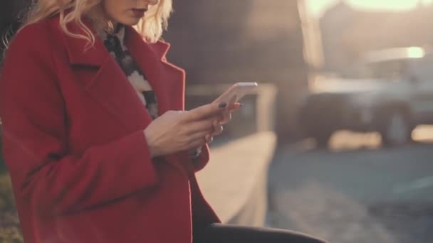 Mujer de negocios con abrigo rojo sentada cerca del centro de negocios y usando phablet de teléfono móvil. Tiro de leva constante . — Vídeos de Stock