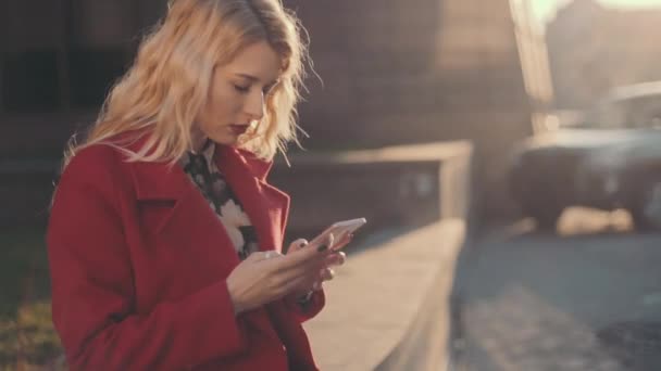 Donna d'affari in cappotto rosso seduto vicino al centro business e utilizzando l'alfabeto del telefono cellulare. Camma costante girato . — Video Stock