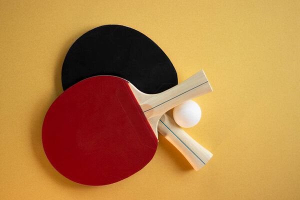Two red table tennis paddles and a white ball arranged on a yellow background.