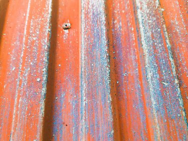 Paslanmış ve yıpranmış metal bir çitin detaylı ticari makro görüntüsü. Canlı turuncu ve mavi boya katmanları yüksek kaliteli endüstriyel tabakalar ve eskimiş mimari materyal detaylarını gösteriyor.