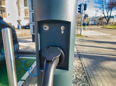 Aktif bir EV 'nin şehir caddesinde şarj olan bir sütunun detaylı görüntüsü. Görüntü, elektrik arabaları ve taşımacılık için kentsel güç altyapısının şarj edici bağlantısını ve modern tasarımını sergiliyor.