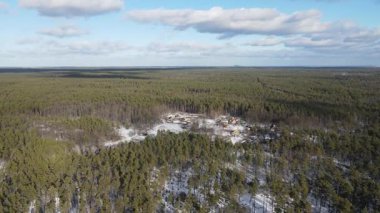 Karlı kozalaklı bir ormanın havadan görünüşü. Bulut gölgeleri ağaçların tepelerinde yavaşça süzülür ve dinamik bir ışık oyunu yaratır. Ormanda küçük bir yerleşim yeri var Belo.. 