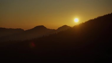 Karanlık dağ siluetleri ve turuncu bir gökyüzüne karşı tepelerle güzel bir gün batımı. Sakin bir akşam atmosferi, günün sonunda dağlarda.