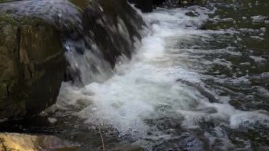 Küçük, doğal bir şelale, taşların üzerinden taşan köpüklü su. Enerji akışı, temiz doku ve ferahlatıcı açık hava atmosferi doğa ve rahatlama temaları için mükemmeldir..