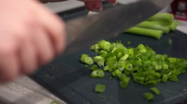 Kesme tahtasına taze soğan dilimleyen bir kadının ellerini mutfak bıçağıyla yakın plan çekiyoruz. Temiz yemek pişirme süreci, doğal malzemeler ve basit yemek hazırlama..