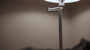 Kamera yukarı doğru eğilir ve sıcak bir iç mekânda sıcak ışık olan modern bir masa lambasını gösterir. Yumuşak aydınlatma, sakin ve rahat bir ev atmosferi yaratır..