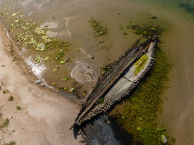 Estonya 'nın Loksa kenti yakınlarındaki tarihi Raketa gemi enkazının yukarıdan aşağıya görüntüsü. Paslı kalıntılar kumlu sahilde duruyor. Temiz ve sığ sularda yeşil yosunlar eşsiz bir deniz manzarası yaratıyor..