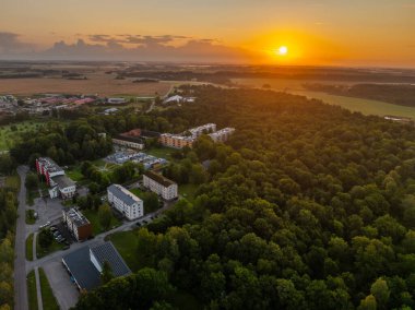 Vinni, Estonya - 10 Ağustos 2025: Vinni 'nin altın saatindeki hava manzarası. Modern apartmanlar, evler ve Vinni anaokulu güneşli bir yaz akşamında yemyeşil orman ve tarlalarla çevrili..
