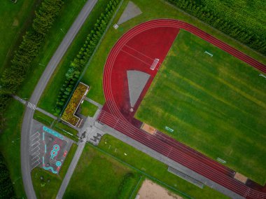 Estonya 'daki Vinni Stadyumu' nun tepeden aşağı görüntüsü. Ağaçlar ve yollarla çevrili kırmızı koşu pisti ve yeşil futbol sahası. Görünür bir kaykay parkı ve park yeri. Yumuşak yayılmış ışıkla aydınlık bir yaz günü