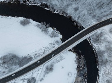Estonya 'nın Tallinn kentindeki Pirita Nehri' nin kışın havadan görünüşü. Karla kaplı bir manzara, kıvrımlı nehri geçen parlak siyah bir yol köprüsü. Arabalar yolda gidiyor..