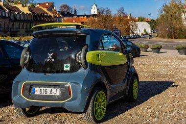 Vilnius, Litvanya - 21 Ekim 2025: Koyu gri ve yeşil XEV YOYO elektrikli araba güneşli Vilnius 'ta eski bir sonbahar gününde park edilmiştir. Arkaplanda tarihi mimari ve kilise kuleleri