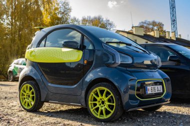 Vilnius, Litvanya - 21 Ekim 2025: Koyu gri ve yeşil XEV YOYO elektrikli araba güneşli Vilnius 'ta eski bir sonbahar gününde park edilmiştir. Arkaplanda tarihi mimari ve kilise kuleleri