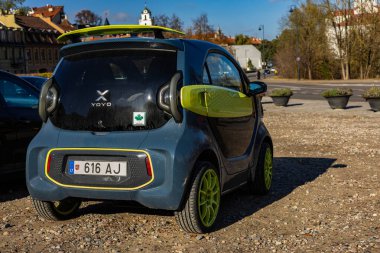 Vilnius, Litvanya - 21 Ekim 2025: Koyu gri ve yeşil XEV YOYO elektrikli araba güneşli Vilnius 'ta eski bir sonbahar gününde park edilmiştir. Arkaplanda tarihi mimari ve kilise kuleleri