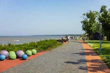 Sillamae - Estonya - 13 Temmuz 2025: Güneşli bir yaz gününde modern Sillamae gezinti alanında yürüyen yaşlı bir adam. Deniz yolu, yeşil park ve Baltık Denizi kıyısı.