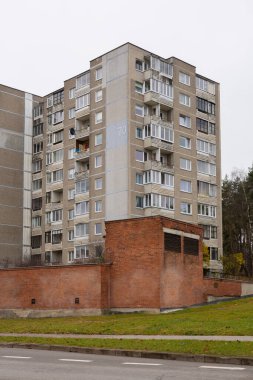Vilnius, Litvanya - 10 Kasım 2025: gri bir sonbahar gününde Sovyet dönemindeki Vilnius apartmanı. Yıpranmış beton paneller, kapalı balkonlar ve kırmızı tuğla bina. Sessiz yerleşim bölgesi