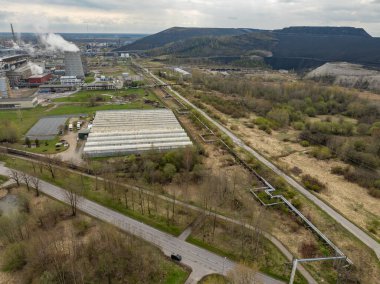 Kohtla-Jarve, Estonya - 20 Nisan 2025: VKG petrol şist fabrikası, buharlı soğutma kuleleri, seralar, boru hatları ve karanlık madencilik tepeleri. Bulutlu bahar havası ham endüstriyel manzarayı vurguluyor