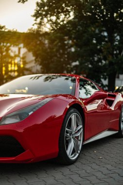 Vilnius, Litvanya - 23 Eylül 2025: Kırmızı Ferrari 488 GTB 2015 akşam ışığında park edildi. Parlak vücut ağaçları ve altın gün batımını yansıtır. Şehir sokak sahnesi, sonbahar yaprakları, lüks süper araba ayrıntıları..