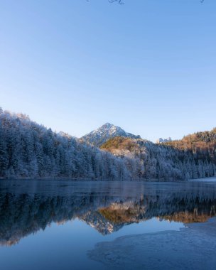Almanya 'nın Bavyera Allgaeu bölgesindeki Alatsee' de güneşli kış atmosferiyle donuk dağlar yansıyor. Yüksek kalite fotoğraf