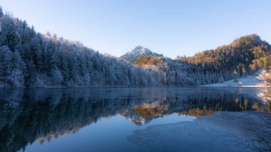 Almanya 'nın Bavyera Allgaeu bölgesindeki Alatsee' de güneşli kış atmosferiyle donuk dağlar yansıyor. Yüksek kalite fotoğraf