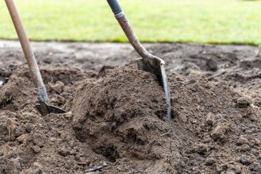 Ahşap saplı paslı bahçe kürekleri el değmemiş yeşil çimlerin ve çim biçme makinesinin yanındaki büyük toprak tümseğe daldırılmış, peyzaj ve bahçe hazırlığı için mükemmel..