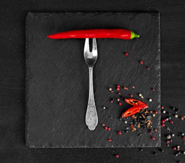 Çatal üzerinde kırmızı biber ve siyah bir yüzeyde kuru baharat bezelyesi. en üstteki görünüm