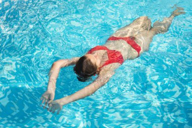 woman in a red swimsuit swims in the pool. The concept of relaxation, sport, spa. Copy space